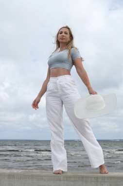 Deniz kenarında poz veren şık, yaz kıyafetli genç bir kadın..