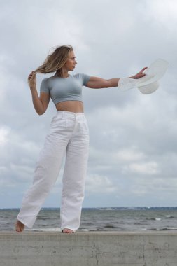 Deniz kenarında poz veren şık, yaz kıyafetli genç bir kadın..