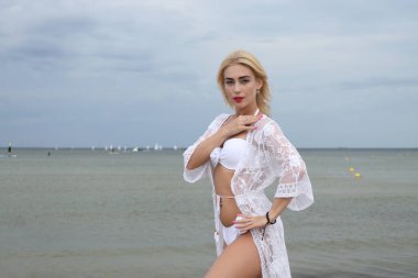 Beyaz bikinili ve dantelli şık bir kadın sahilde zarifçe poz veriyor..