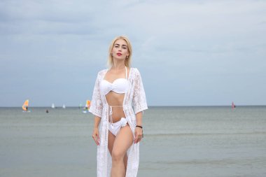 Beyaz bikinili ve dantelli şık bir kadın sahilde zarifçe poz veriyor..