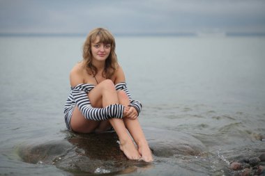 Deniz kıyısındaki kayalarda poz veren şehvetli genç kadın..