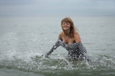 Çizgili tişörtlü çekici kız okyanusta su sıçratmaktan hoşlanıyor.
