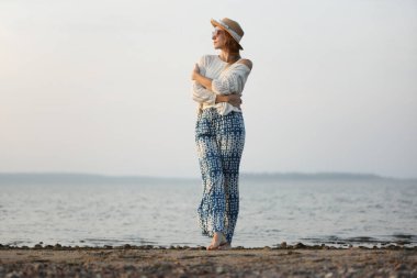 Rahat bir kadın gün batımında sakin bir sahil gezintisi yapıyor.