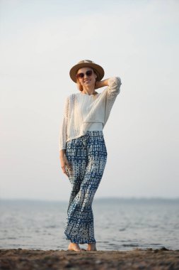 Rahat bir kadın gün batımında sakin bir sahil gezintisi yapıyor.