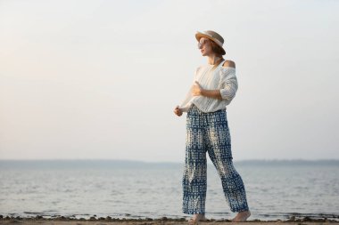 Rahat bir kadın gün batımında sakin bir sahil gezintisi yapıyor.