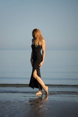 Siyah elbiseli zarif bayan deniz kenarında yalınayak dolaşıyor..