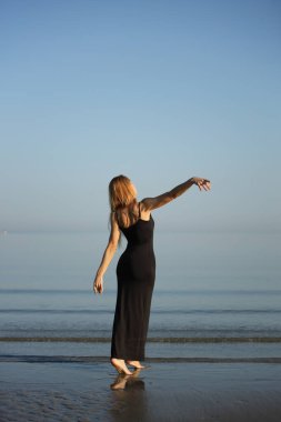 Siyah elbiseli zarif bayan deniz kenarında yalınayak dolaşıyor..