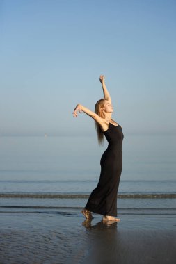 Siyah elbiseli zarif bayan deniz kenarında yalınayak dolaşıyor..