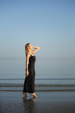 Siyah elbiseli zarif bayan deniz kenarında yalınayak dolaşıyor..