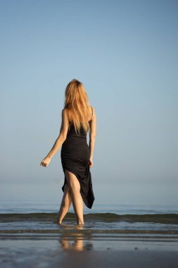 Siyah elbiseli zarif bayan deniz kenarında yalınayak dolaşıyor..