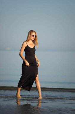 Siyah elbiseli zarif bayan deniz kenarında yalınayak dolaşıyor..