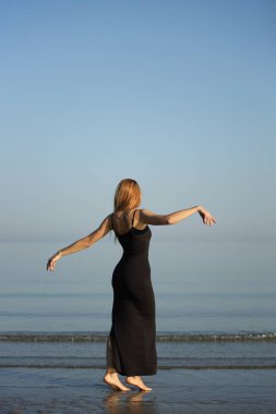 Siyah elbiseli zarif bayan deniz kenarında yalınayak dolaşıyor..