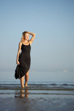 Siyah elbiseli zarif bayan deniz kenarında yalınayak dolaşıyor..