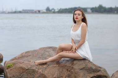 Deniz kenarındaki genç, narin kadın. Kıyafetler içinde poz veriyor.