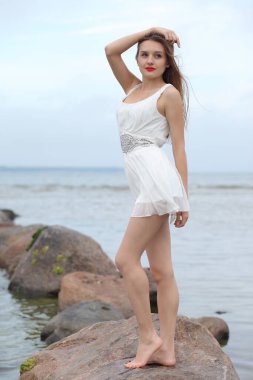 Deniz kenarındaki genç, narin kadın. Kıyafetler içinde poz veriyor.