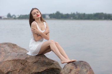 Deniz kenarındaki genç, narin kadın. Kıyafetler içinde poz veriyor.