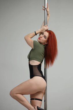 Gülümseyen kızıl saçlı bir kadın zarif bir şekilde direk dansı yapıyor.