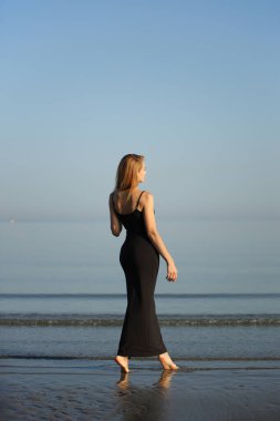 Siyah elbiseli zarif bayan deniz kenarında yalınayak dolaşıyor..