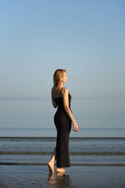 Siyah elbiseli zarif bayan deniz kenarında yalınayak dolaşıyor..