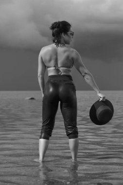 Kendine güvenen bir kadın dramatik gökyüzünün altında suyun içinde duruyor..