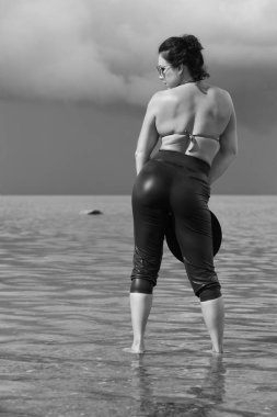 Kendine güvenen bir kadın dramatik gökyüzünün altında suyun içinde duruyor..