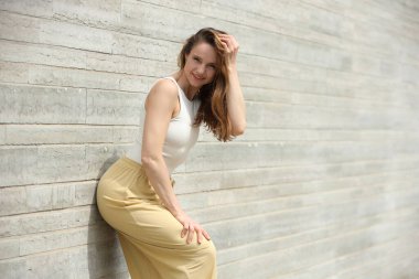 Modern duvara yaslanmış, kendine güveni tam, hafif elbiseli bir kadın.