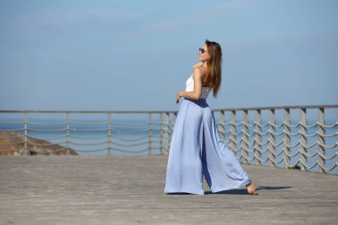 Şık bir kadın iskeledeki huzurlu deniz manzarasının tadını çıkarıyor..