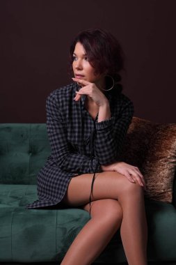 Kanepede oturan şık bir kadın, düşünceli bir ifadeyle poz veriyor..