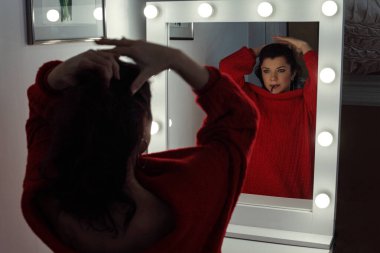 Güzel bir kadın saçını düzeltiyor ve aynanın yanında poz veriyor..