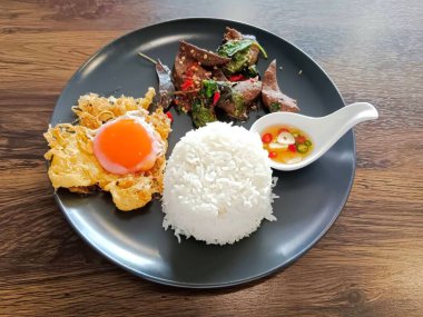 Buharda pilav, sahanda yumurta, taze biberli kızarmış domuz ciğeri ve ahşap masada koyu renkli seramik tabakta servis edilen beyaz kaşıkta balık sosu.