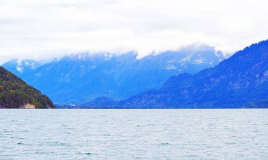  Bulutlu mavi gökyüzü arka planının altında Interlaken gölü kıyısındaki büyük dağ evleri