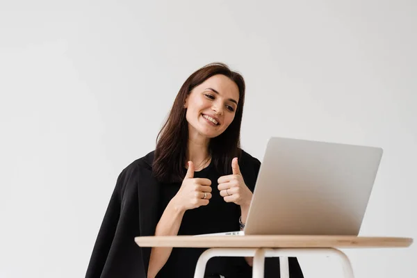 Cheerful woman showing thumbs up to her colleagues and friends on video meeting. Happy girl with works on laptop and rejoices in the implementation of successful project