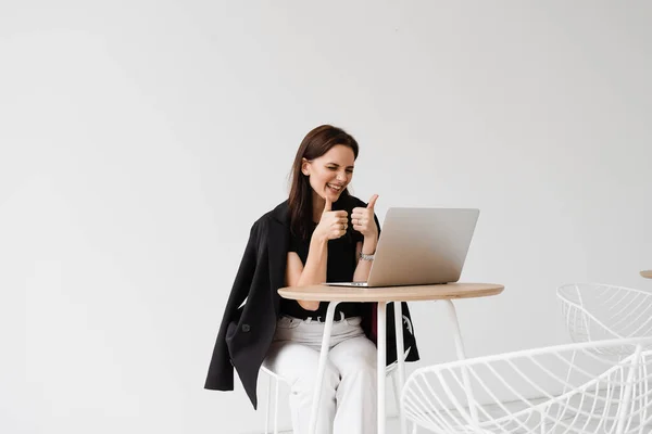 Happy girl with laptop showing thumbs up on video communication with friends. Successful business woman works remotely and laughs with colleagues in online video meeting