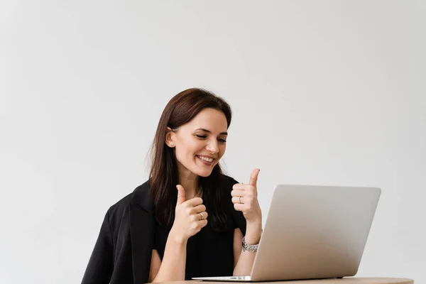 Happy girl with laptop showing thumbs up on video communication with friends. Successful business woman works remotely and laughs with colleagues in online video meeting