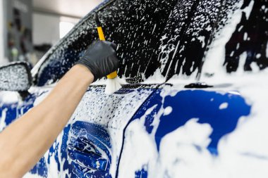 Araba yıkama servisinde köpüklü el fırçası. Araba yıkama işçisi bir arabayı yıkar.