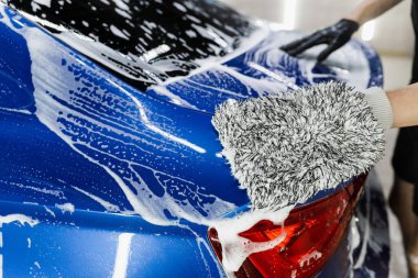 Araba yıkama makinesi oto yıkama servisinde elle köpük yıkıyor. Mikrofiber eldivenle el yıkama ve garajda köpüklü araba gövdesi.