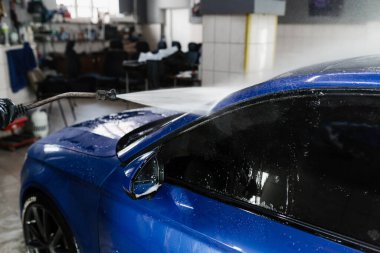 Garajda köpüğü temizlemek için arabaya su püskürtmek. Araba servisinde yıkama işlemi. Araba yıkama makinesi araba yıkama için su dolduruyor.