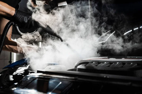 Process of steam cleaning car engine from dust and dirt. Steaming washing of motor of auto in detailing auto service