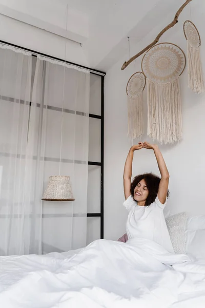 非洲裔美国妇女醒来 享受着早晨的愉快 穿着睡衣的非洲女孩在床上抽筋 在家里举手 — 图库照片
