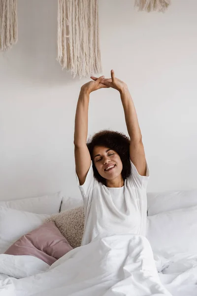 非洲裔美国妇女醒来 享受着早晨的愉快 穿着睡衣的非洲女孩躺在舒适的床上 双手高举在家里 — 图库照片