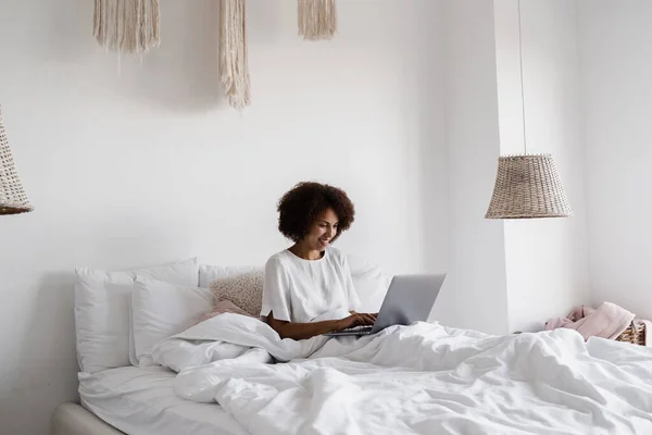 African girl manager with laptop have online video meeting with colleagues and business partners in cozy bed at home in the morning. Team discussion trends and tasks