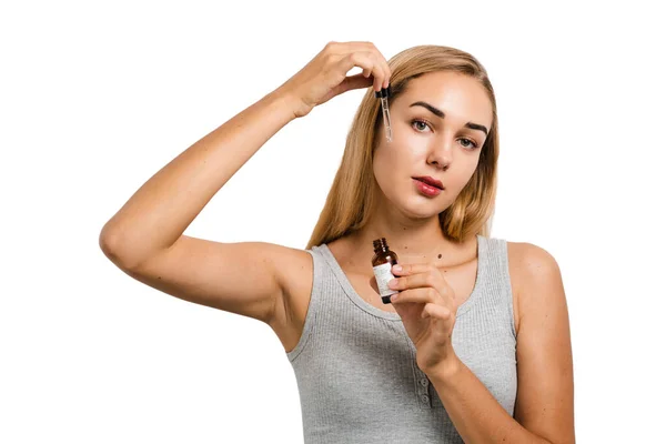 Young woman with face serum pipette for acne treatment and wrinkle smoothing. Girl applies face serum to her face with pipette on white background
