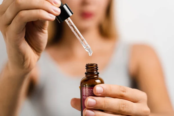 Face serum pipette close-up in hands of attractive girl on white background. Girl applies face serum to her face with pipette on white background