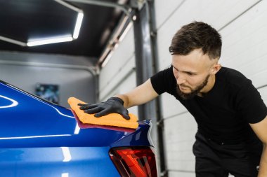 Temizlikçi adam araba yıkadıktan sonra araba kurutur. Otomobil servisinde mikrofiberle kurutulan el arabası.