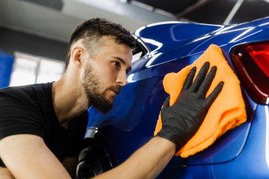 Temizlikçi adam araba yıkadıktan sonra araba kurutur. Otomobil servisinde mikrofiberle kurutulan el arabası.