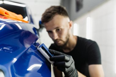 Otomobil servisinde sünger kullanılarak seramik koruyucu kaplama uygulanması. Araba servisi çalışanı arabayı çiziklerden korumak için seramik kaplama uygular.