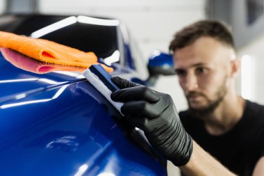 Otomobil servisinde sünger kullanılarak seramik koruyucu kaplama uygulanması. Araba servisi çalışanı arabayı çiziklerden korumak için seramik kaplama uygular.