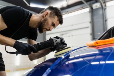 Yörünge cilasıyla araba cilalaması, çizikleri silmek için. Otomobil servisi çalışanı araba için son cilalamayı yapıyor