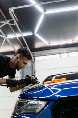 Yörünge cilasıyla araba cilalaması, çizikleri silmek için. Otomobil servisi çalışanı araba için son cilalamayı yapıyor