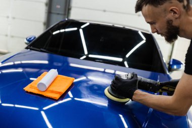 Yörünge cilasıyla araba cilalaması, çizikleri silmek için. Otomobil servisi çalışanı araba için son cilalamayı yapıyor